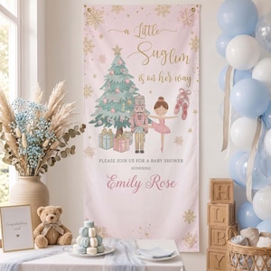 May include: A vertical pink banner featuring a Christmas tree, a nutcracker, a ballerina, and ballet slippers. The text reads: A Little Suglim is on her way, PLEASE JOIN US FOR A BABY SHOWER HONORING Emily Rose. Gold snowflakes decorate the edges.