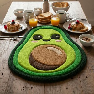 May include: A whimsical avocado-shaped rug in shades of green and brown sits on a wooden table, surrounded by breakfast items. The rug features a smiling face and is the centerpiece of a breakfast setting with pancakes, juice, and coffee.