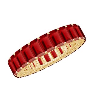 Könnte beinhalten: Ein goldfarbener Ring mit einer Reihe rechteckiger, tiefroter Edelsteine. Die Edelsteine sind eng aneinandergereiht und bilden ein durchgehendes Farbband. Das Ringband hat ein aufwendiges, offenes Design.