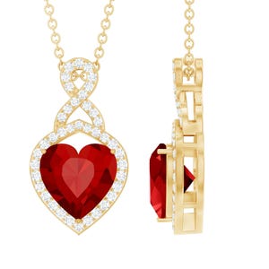 May include: A gold pendant necklace with a heart-shaped, deep red gemstone. The heart is encircled by a halo of small, clear gemstones. The necklace chain and the pendant's upper design are also gold-coloured.