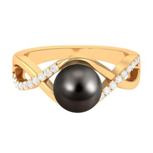 May include: A gold ring featuring a large, dark gray pearl at the center. The ring's band has an interwoven design, with small, clear gemstones set along the edges, creating a sparkling accent.