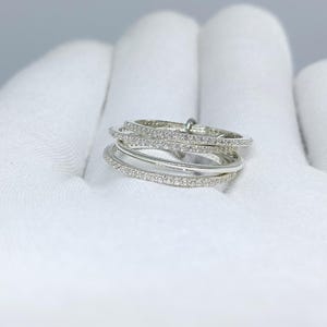 Peut inclure: Une bague en argent composée de plusieurs anneaux, chacun orné de petits pierres précieuses transparentes. Les anneaux sont superposés, créant un design unique et complexe. La bague est posée sur un fond blanc.