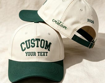 Pode incluir: Dois bonés de beisebol com copa cor de creme e aba verde-escura. O boné da frente exibe o texto bordado CUSTOM YOUR TEXT em verde-escuro. O boné de trás apresenta a palavra bordada custom e o número 2026.