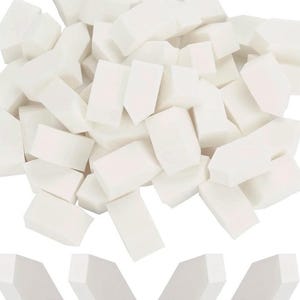 Op de afbeelding: Een stapel witte, rechthoekige make-up sponsjes met schuine randen. De sponsjes zijn dicht op elkaar gepakt, met enkele losse sponsjes verspreid aan de onderkant. De afbeelding is helder verlicht, wat de schone, witte kleur van de sponsjes benadrukt.