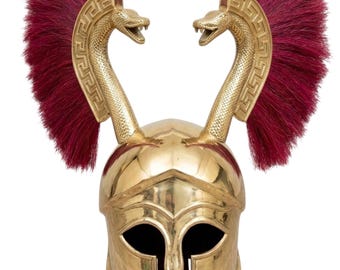 May include: A polished gold-tone metal helmet featuring two upright snake figures on the sides. Each snake is adorned with a Greek key pattern and is flanked by a large, vibrant deep red brush crest that extends upwards from the helmet base.