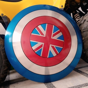 Puede incluir: Un escudo redondo con un diseño azul, plateado y rojo. El escudo presenta un diseño de la Union Jack en el centro, rodeado de anillos concéntricos rojos, plateados y azules. El escudo es probablemente de metal.