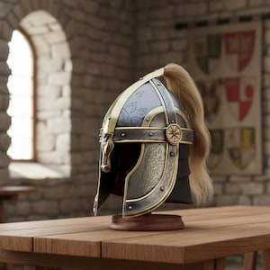 May include: A detailed medieval helmet with gold and silver accents, featuring intricate designs and a blonde ponytail. The helmet is displayed on a wooden stand, set against a backdrop of a stone wall and a tapestry.