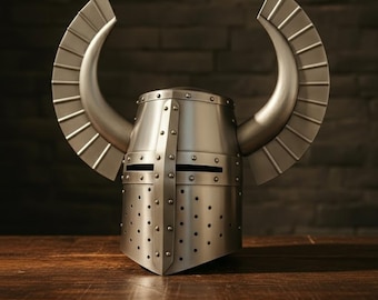 May include: A silver-colored medieval helmet with curved, wing-like protrusions. The helmet features a riveted construction with small, evenly spaced holes and horizontal eye slits. It sits on a wooden surface against a dark brick background.