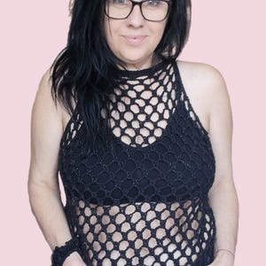 Può includere: Top nero all'uncinetto a trama aperta con scollatura all'americana. Il top è indossato sopra un capo intimo nero. La persona indossa jeans blu e un braccialetto all'uncinetto abbinato. Lo sfondo è rosa chiaro.