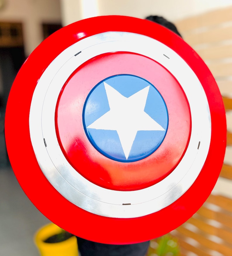 May include: A circular shield with a red border, a white band, and a blue central disc. A white star is in the middle. This shield is a replica of Captain America's shield.