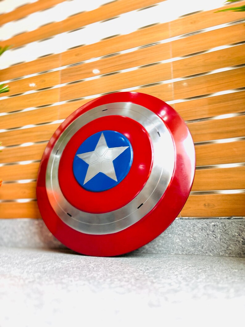 May include: A round shield in red, white, and blue, featuring a silver trim and a central white star. The design is iconic, resembling a superhero's shield, with a diameter of approximately 76 cm.