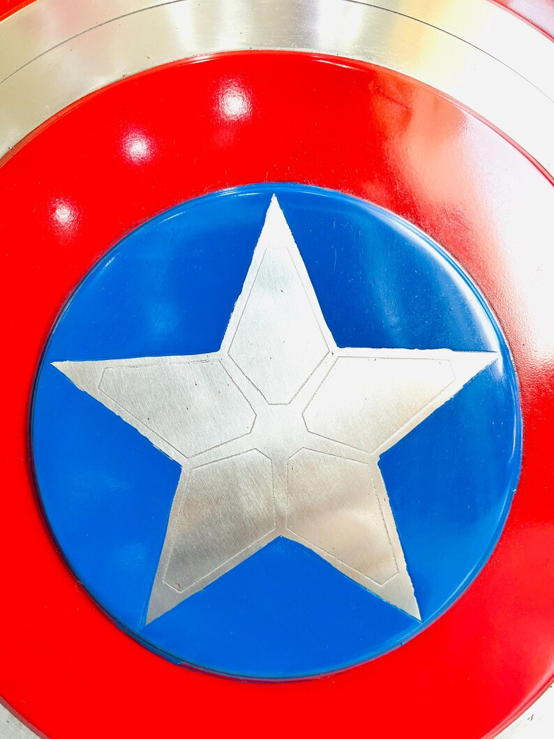 May include: A close-up of a shield with a red outer ring, a silver inner ring, and a blue center. A large, silver five-pointed star is in the center of the blue circle. The shield has a glossy finish.