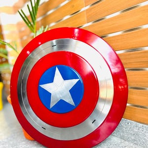 May include: A round shield in red, white, and blue, featuring a silver ring and a white star on a blue circle. The shield is made of metal.