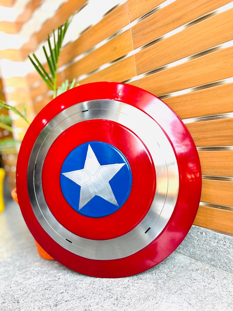 May include: A round shield in red, white, and blue, featuring a silver ring and a white star on a blue circle. The shield is made of metal.