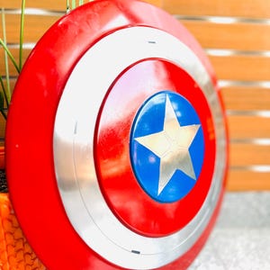 May include: A circular shield in red, white, silver, and blue, featuring a star emblem. The shield has a red outer ring, a white inner ring, and a silver band. The centre has a blue circle with a gold star.