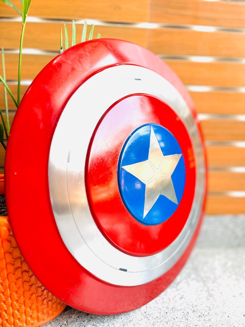 May include: A circular shield in red, white, silver, and blue, featuring a star emblem. The shield has a red outer ring, a white inner ring, and a silver band. The centre has a blue circle with a gold star.
