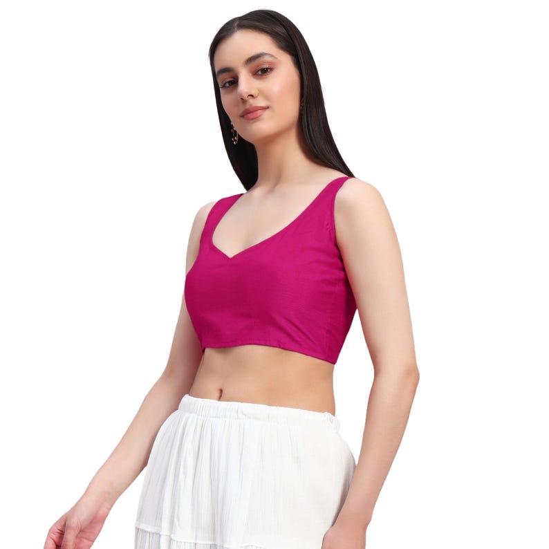 Puede incluir: Un top magenta sin mangas con cuello en V. El top es de color liso y parece estar hecho de una tela suave. La modelo lleva el top con una falda blanca.