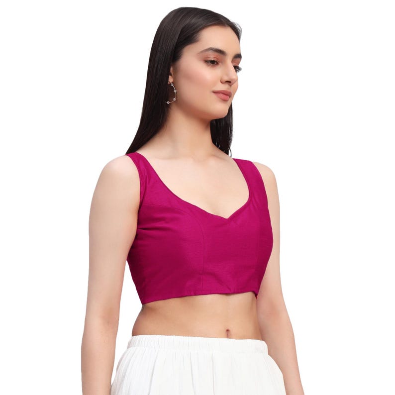 Puede incluir: Un top sin mangas magenta con escote en V. El top est&aacute; hecho de una tela lisa. La modelo lleva el top con pantalones blancos y pendientes dorados.