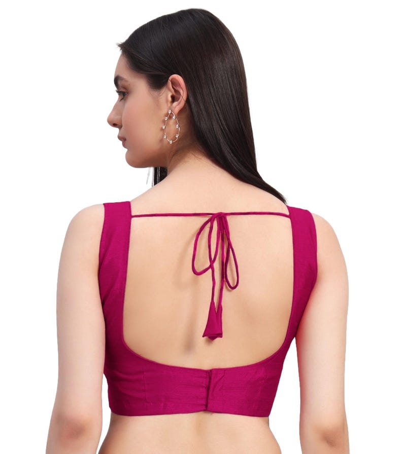 Puede incluir: Una blusa sin mangas de color magenta con cuello cuadrado y cierre de lazo en la espalda. La blusa est&aacute; hecha de una tela suave y tiene un dise&ntilde;o simple y elegante. La parte trasera de la blusa es visible, mostrando el detalle del lazo.