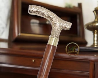 May include: A wooden walking cane with a silver-colored, ornate handle. The handle features a detailed floral design. The cane has a brass collar and a dark brown wooden shaft. The cane is a classic accessory.