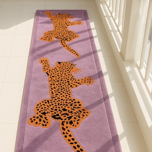 Puede incluir: Dos alfombras rectangulares moradas con un diseño de leopardo naranja y negro. Las alfombras están colocadas sobre un suelo de baldosas blancas, cerca de una ventana con barandillas blancas.