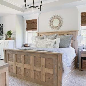 Può includere: Un letto in legno chiaro con testiera e pediera. Il letto è in legno naturale e ha una trapunta e cuscini grigio chiaro. Un lampadario nero pende dal soffitto.