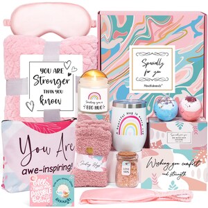 May include: A pink gift box filled with self-care items. Includes a blanket, eye mask, candle, tumbler, bath bombs, socks, and a cosmetic bag. The box has text that says "You are stronger than you know" and "You are awe-inspiring!"