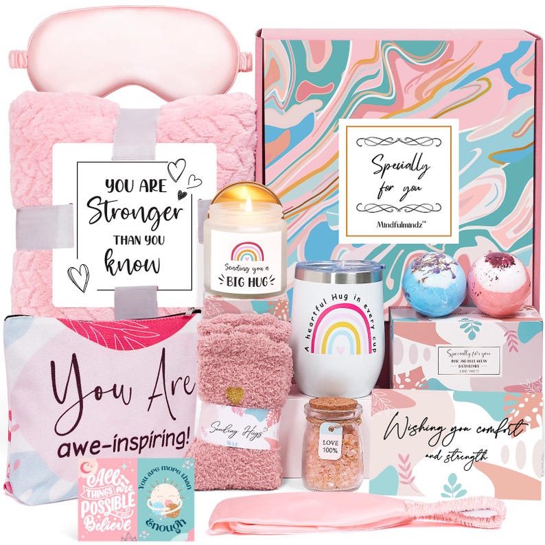 May include: A pink gift box filled with self-care items. Includes a blanket, eye mask, candle, tumbler, bath bombs, socks, and a cosmetic bag. The box has text that says "You are stronger than you know" and "You are awe-inspiring!"
