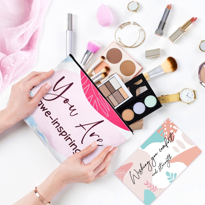 May include: A cosmetic bag with the words "You Are awe-inspiring" in a script font. The bag is open, revealing makeup brushes, eyeshadow palettes, and other beauty products. A card with the words "Wishing you comfort and strength" is also visible.