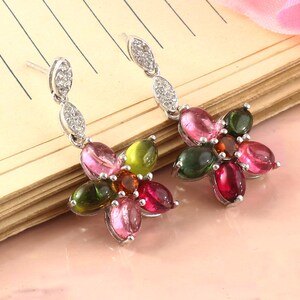 Könnte beinhalten: Silberne Ohrringe mit floralem Design. Jeder Ohrring hat eine Ansammlung farbiger Edelsteine in Rosa-, Grün- und Rottönen, mit einem kleinen, länglichen, diamantbesetzten Akzent über der Blume.