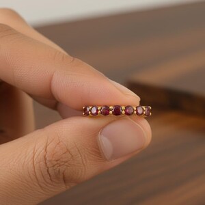 Könnte beinhalten: Ein Goldring mit einer Reihe von sechs rund geschliffenen, tiefroten Edelsteinen in einer gemeinsamen Krappenfassung. Der Ring weist eine polierte metallische Oberfläche und eine gleichmäßige kreisförmige Anordnung der Steine auf.