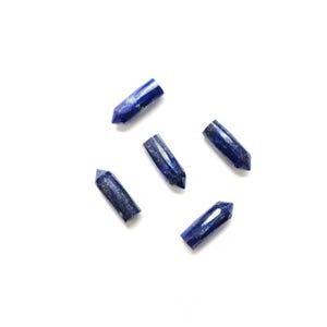 Op de afbeelding: Vijf gepolijste lapis lazuli kristallen punten worden getoond tegen een witte achtergrond. De kristallen zijn diepblauw met gouden vlekken, elk met een puntig uiteinde. Deze edelstenen worden vaak gebruikt voor genezing en meditatie.