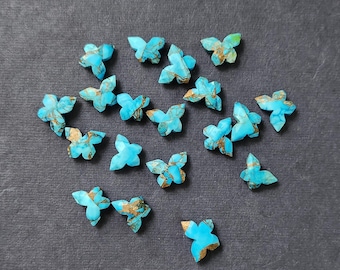 May include: A collection of turquoise butterfly-shaped gemstones with gold-colored veining. The gemstones are arranged on a dark gray surface, showcasing their vibrant blue color and intricate details. These gemstones are ideal for jewelry making.