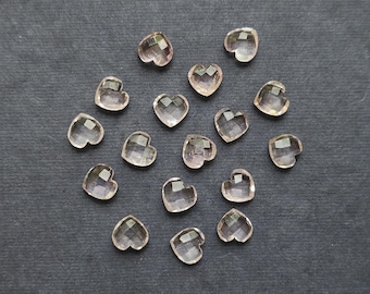 May include: A collection of faceted, heart-shaped gemstones in a pale pink hue. The gemstones are scattered on a dark gray surface, showcasing their clear, sparkling appearance. These heart-shaped stones are ideal for jewelry making or craft projects.