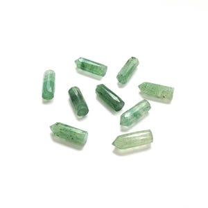 Może przedstawiać: Kolekcja małych, zielonych kryształowych szpiców rozrzuconych na białej powierzchni. Kryształy mają fasetowany, sześciokątny kształt i różnią się nieznacznie odcieniem, od jasnej do ciemnej zieleni. Kryształy mają około 2.5 cm długości.