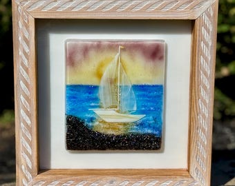 May include: A framed glass art piece depicting a sailboat on a blue sea with a yellow and purple sunset. The sailboat is white, and the frame is light brown with a textured design.