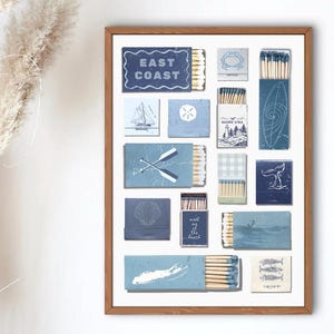 Puede incluir: Una impresión enmarcada con varios diseños de cajas de cerillas con temas costeros. Las cajas de cerillas son en tonos azules y blancos, con ilustraciones de veleros, remos y el texto "EAST COAST" y "meet at the beach".