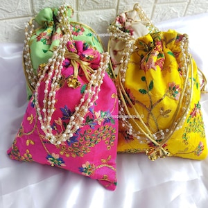 May include: Four colorful drawstring bags with floral embroidery and pearl-like beaded drawstrings. The bags are in shades of pink, yellow, green, and cream. The text "Stylespeaksjaipur" is visible on the bags.