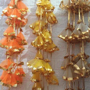 May include: Decorative hanging ornaments in shades of orange, yellow, and cream. Each ornament features a layered, bell-shaped design with gold trim. The ornaments are suspended from thin gold cords, creating a festive and elegant display.