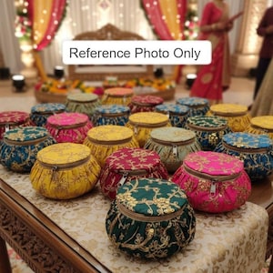 May include: A collection of colorful, round, fabric-covered containers with gold embroidery and zipper closures. The containers are in various colors, including yellow, pink, teal, and green, and are arranged on a table with a decorative cloth. The text "Reference Photo Only" is visible.