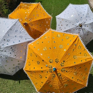 Peut inclure: Vue aérienne de quatre parapluies décoratifs ouverts. Deux sont blancs avec des découpes florales et des accents argentés, et deux sont jaunes avec des détails similaires. Chaque parapluie a un bord festonné.