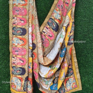 Pode incluir: Um tecido colorido com padrões e enfeites intrincados. O tecido apresenta um design repetitivo de figuras e formas em tons de rosa, azul, laranja e amarelo, com uma borda dourada. O texto "Stylespeaksjaipur" é visível.