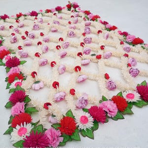 May include: A decorative floral garland featuring a lattice design. The garland is adorned with a variety of flowers in shades of pink, red, and white, set against a cream-colored backdrop. Green leaves accent the floral arrangement.