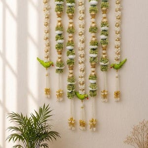Puede incluir: Un colgante de pared con seis hileras verticales de guirnaldas florales blancas y verdes intercaladas con cuentas esféricas de color dorado. Tres figuras de loros verdes están unidas a las hileras. El texto Reference Photo Only es visible.