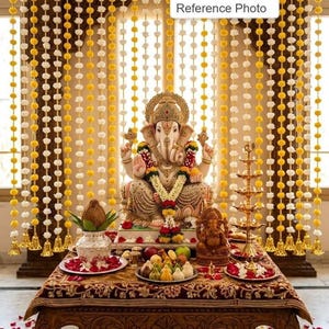Pode incluir: Uma exibição detalhada com uma estátua de Ganesha, adornada com guirlandas, colocada sobre uma mesa com oferendas de frutas e doces. O fundo inclui cordas decorativas de flores brancas e amarelas, criando um ambiente festivo.