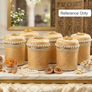 May include: Six decorative, cylindrical jars with gold-coloured lids and bases. The lids are topped with a gold floral design and trimmed with lace and pearls. The jars are surrounded by small glass bowls of nuts and dried fruit.