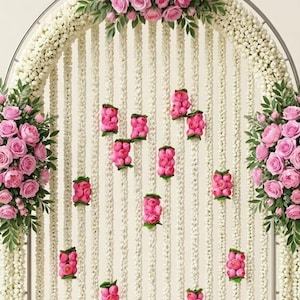 May include: A metal arch decorated with long, vertical strands of small white flowers. Clusters of pink roses and green leaves are attached to the top and sides. Small groupings of pink flowers are interspersed along the white floral strands.