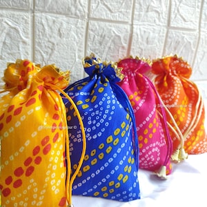May include: A collection of colorful drawstring bags in yellow, blue, pink, and orange. Each bag features a unique pattern of dots and lines, with gold trim and drawstrings. The bags are arranged in a row, showcasing their vibrant colors and designs.