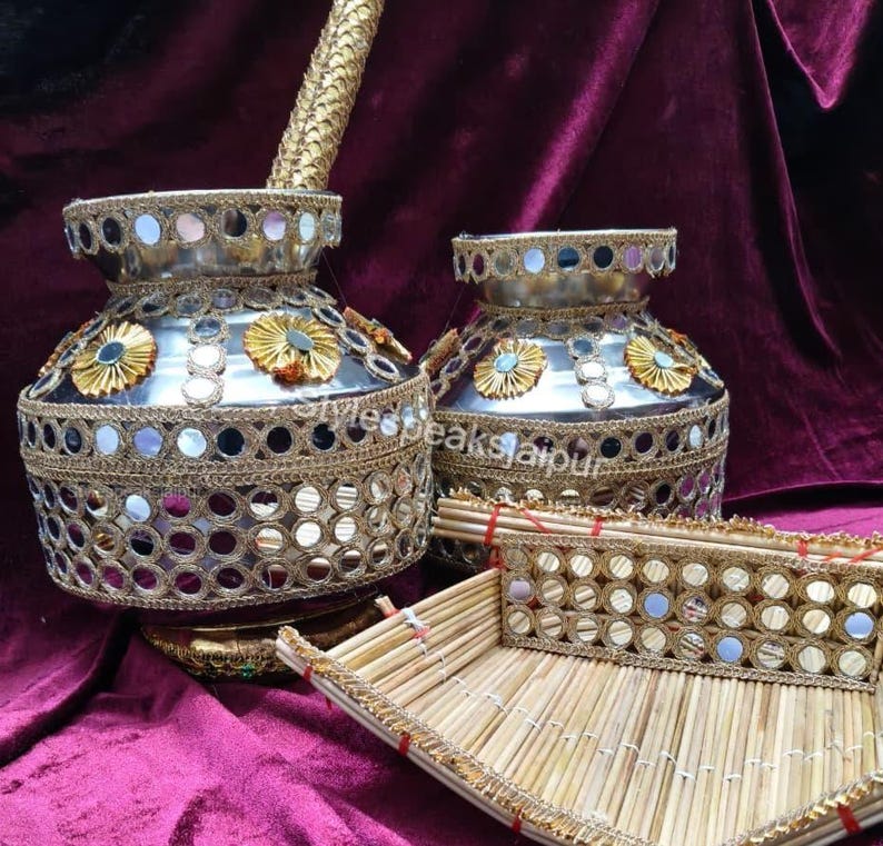 Puede incluir: Jarr&oacute;n decorativo plateado con intrincados adornos dorados y espejados. Los jarrones presentan detalles florales y van acompa&ntilde;ados de una bandeja de bamb&uacute;, todo sobre un fondo burdeos. Conjunto decorativo.