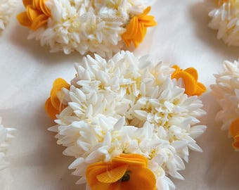 May include: Close-up of several white flower garlands with yellow accents. The garlands are round and have a textured appearance, with the yellow accents adding a pop of color. The flowers are arranged in a circular pattern.